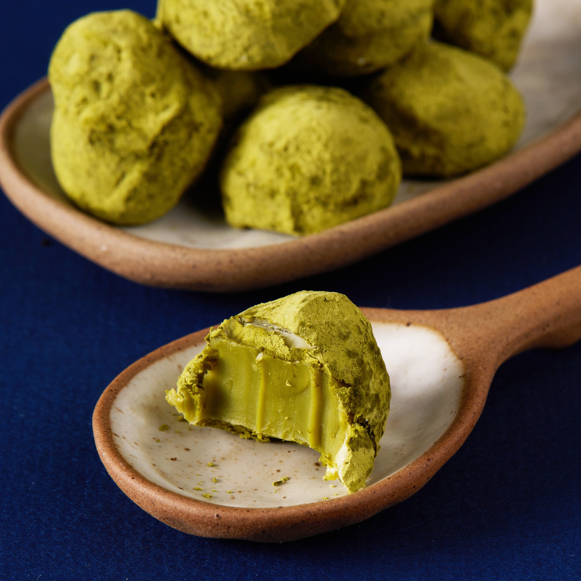 Green Matcha tea truffles on a wooden spoon with a plate of truffles in the background.