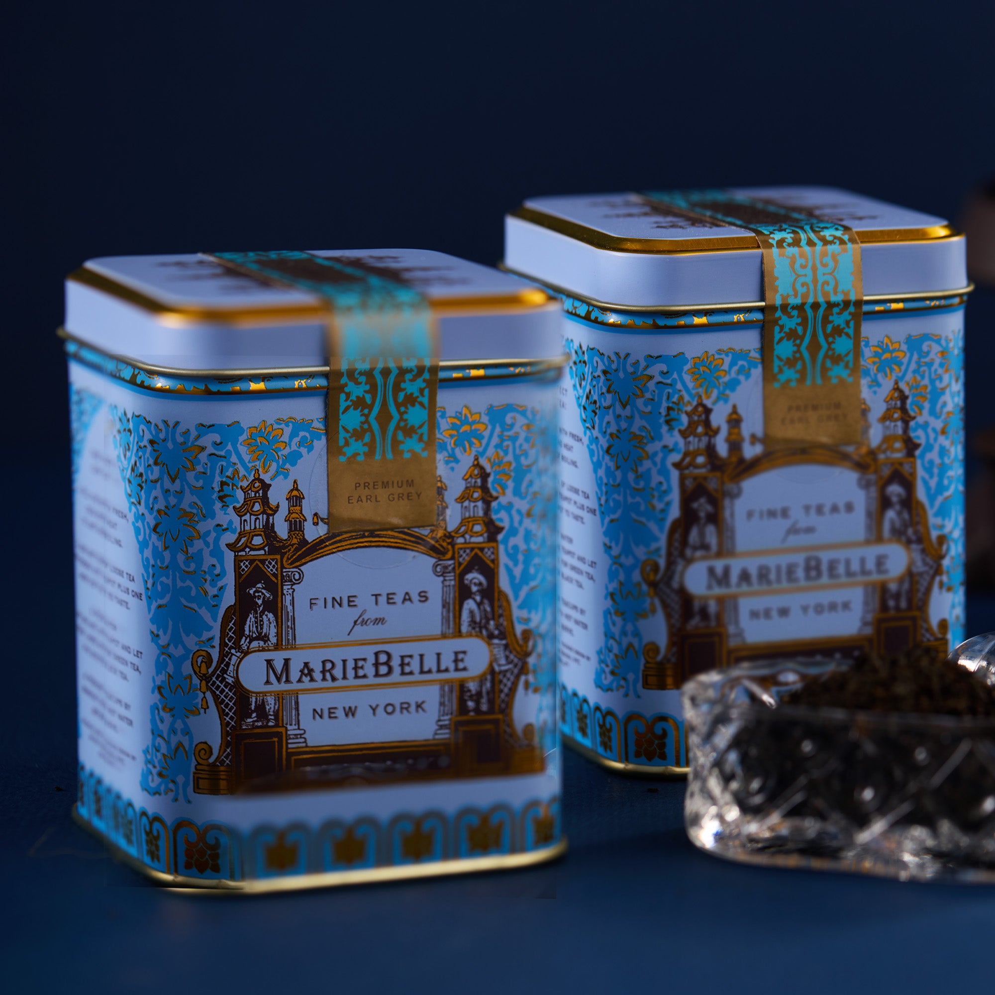 Two MarieBelle tea tins with decorative labels on a dark background
